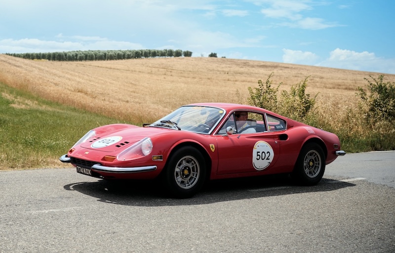 red Ferrari racing past a field of wheat.