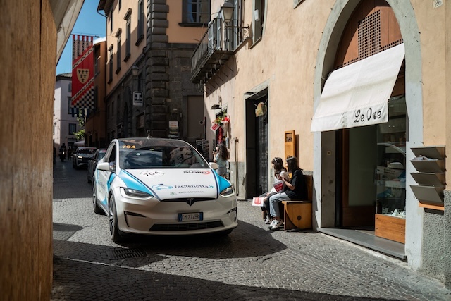 A white Tesla driving through a small Italian street.