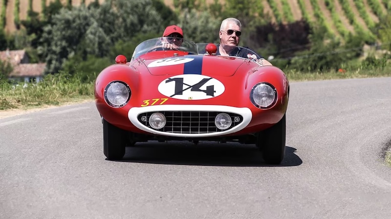 Two men driving in a red Ferrari.