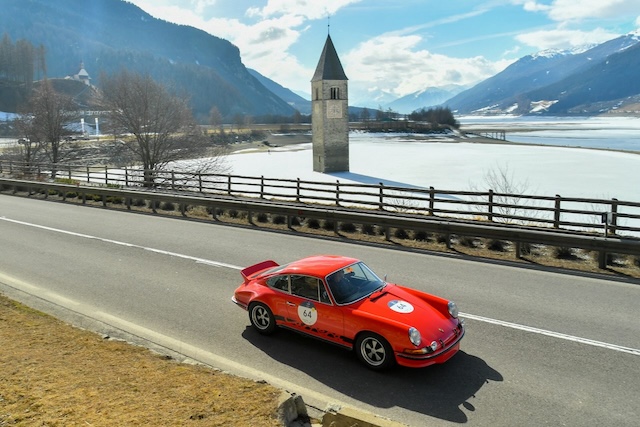 Red Porsche driving past a lake in Italy.